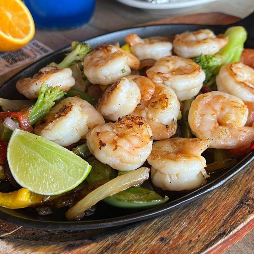Sizzling shrimp fajitas with colorful bell peppers, onions, broccoli, and a lime wedge on a black skillet.